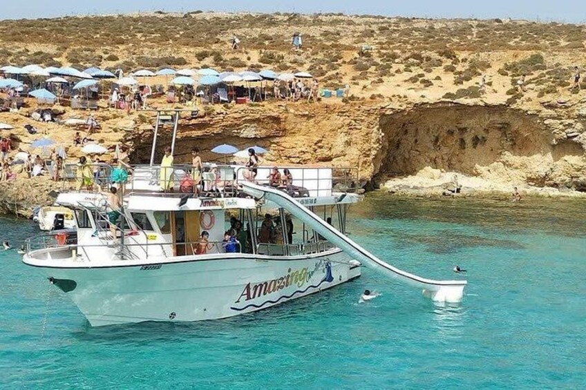 A boat named 'Amazoni' docked at a beach with people on the shore and a rocky cliff in the background. 3