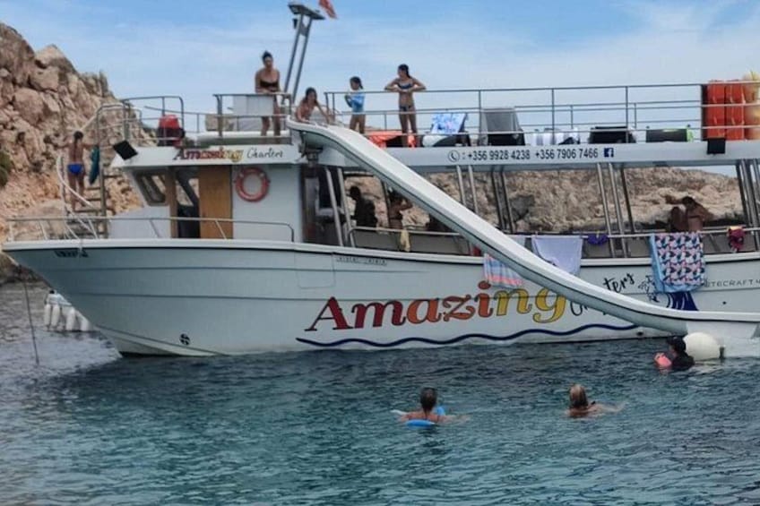 A boat with people swimming in the water and a rocky shore in the background. 1