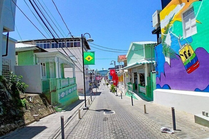Une rue pavée bordée de bâtiments aux couleurs vives, un drapeau brésilien et une fresque représentant une scène de plage. 5