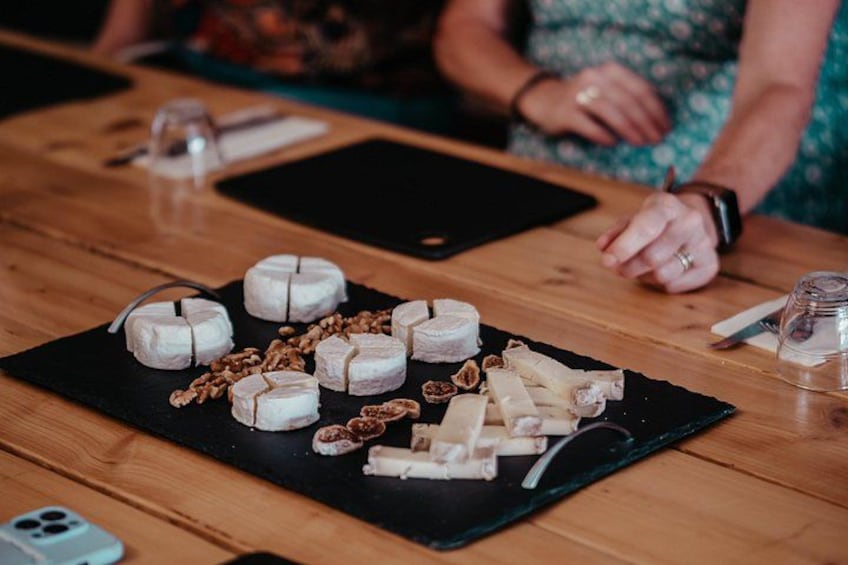 A wooden table with a black placemat holding various cheeses and nuts. 4