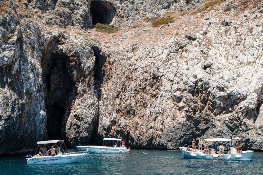 A rocky coastline with boats anchored near a cave entrance. 2