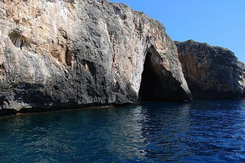A rocky coastline with a cave entrance and clear blue water. 3