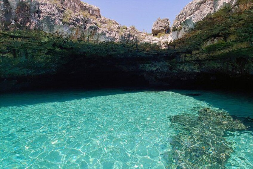 A clear turquoise sea, rocky cliffs, and a cave entrance. 1