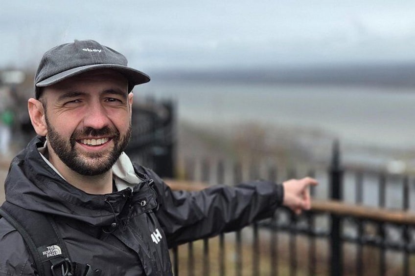 A person wearing a black jacket and a cap, pointing towards the water. 3