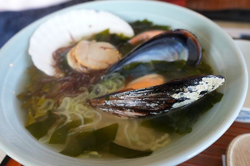 A bowl of seafood soup with mussels, clams, and noodles. 4