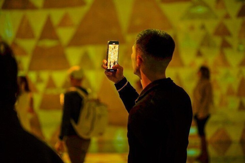 A person holding a smartphone, possibly taking a photo, with a geometric pattern in the background. 5