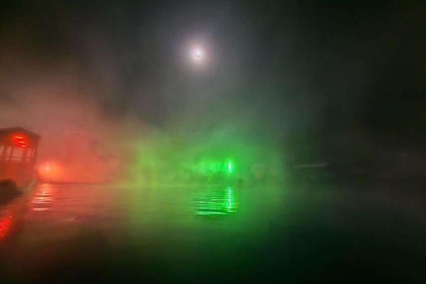 Une scène nocturne brumeuse, avec une lumière verte se reflétant sur la surface de l’eau. 4