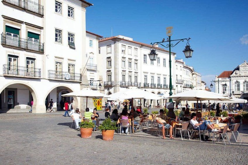 A public square with outdoor seating, historic buildings, and people walking. 2
