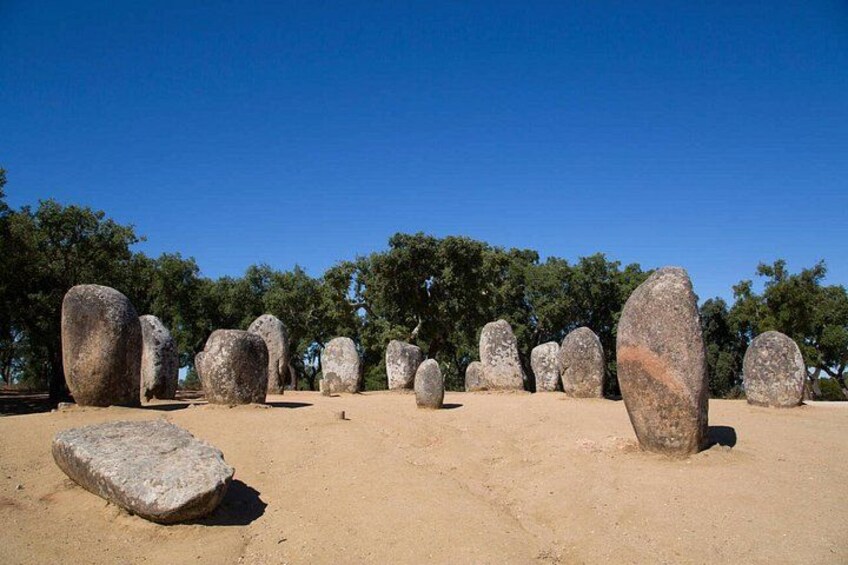 A series of large standing stones in a clear, open field with trees in the background. 5