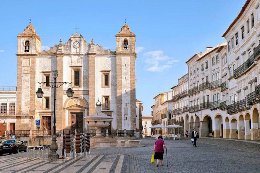A historic church with two bell towers, a cobblestone street, and a pedestrian. 3