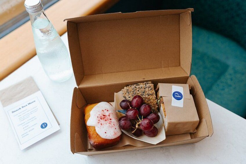 A cardboard box with a pastry, grapes, and a bottle of water on a table. 4