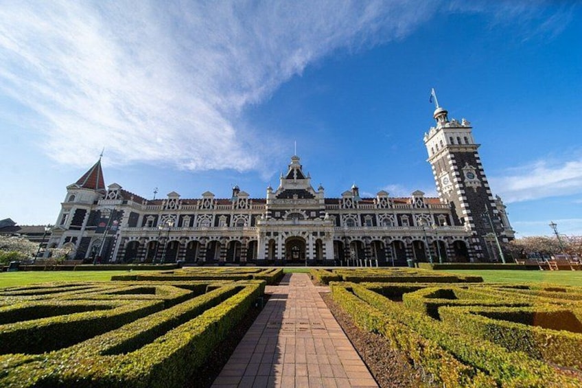 A large, historic building with a central dome and a tall tower, surrounded by well-manicured gardens and a clear sky. 5