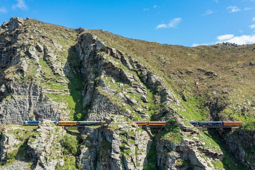 Un tren sobre una vía en la montaña, con acantilados rocosos y vegetación escasa. 3