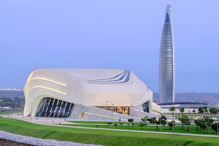 A modern architectural building with a unique curved roof, surrounded by a well-maintained lawn and a tall skyscraper in the background. 4