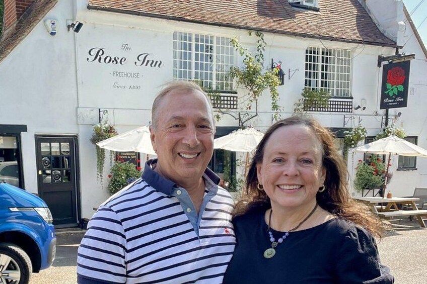 A man and a woman standing in front of The Rose Inn, a white building with a black door and windows. 2