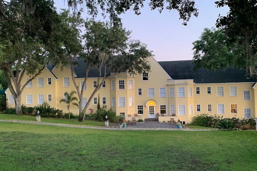 A large yellow building with a symmetrical facade, surrounded by lush green lawns and mature trees. 1