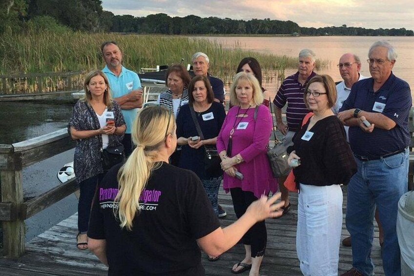 A group of people on a wooden dock by a body of water, some holding drinks. 2