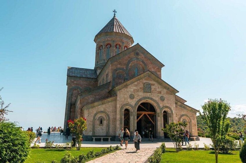 Een grote kerk met een opvallende klokkentoren, omgeven door een verzorgde tuin en een heldere lucht. 1
