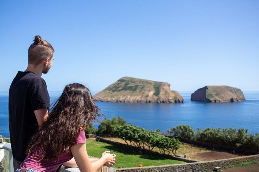 Una pareja contemplando un paisaje costero con zonas verdes y un viñedo. 5