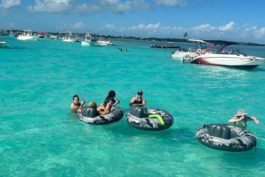 People floating on intertubes in turquoise water with boats in the background. 2