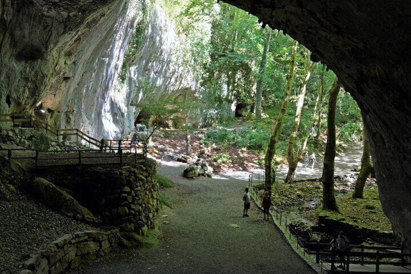 A cave entrance with a pathway leading inside, surrounded by trees and a waterfall. 2