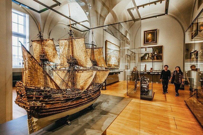 En stor modell av ett fartyg i ett museum, utställd i ett glasmontr och omgiven av besökare. 4
