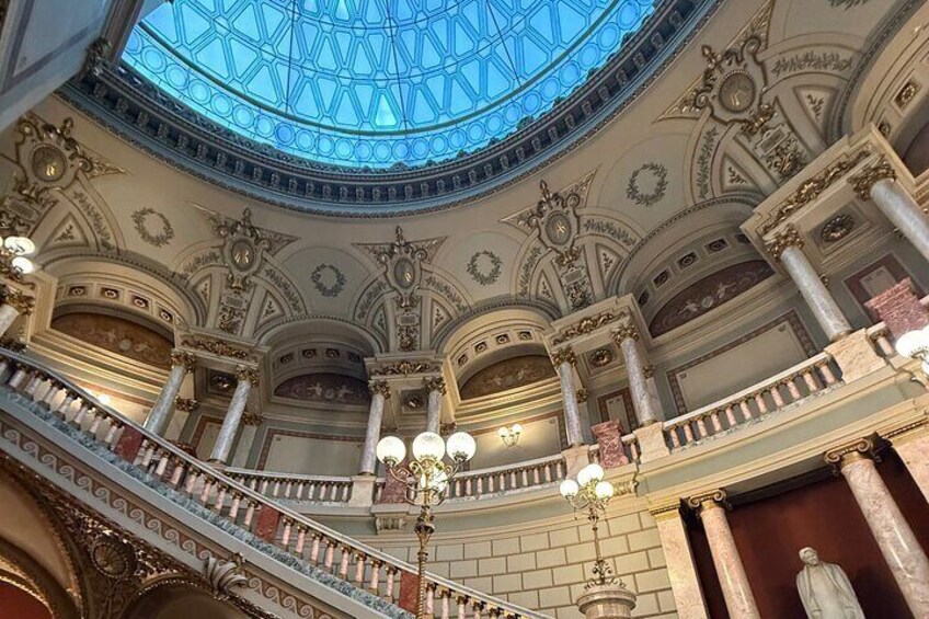 An ornate interior with a glass dome ceiling, columns, and a statue. 4