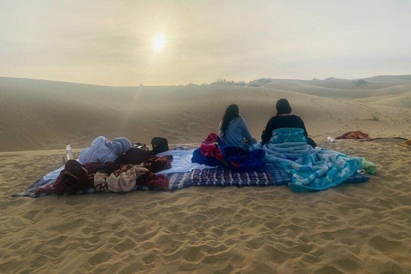 Personas sentadas sobre una manta en un desierto con dunas de arena al fondo. 3