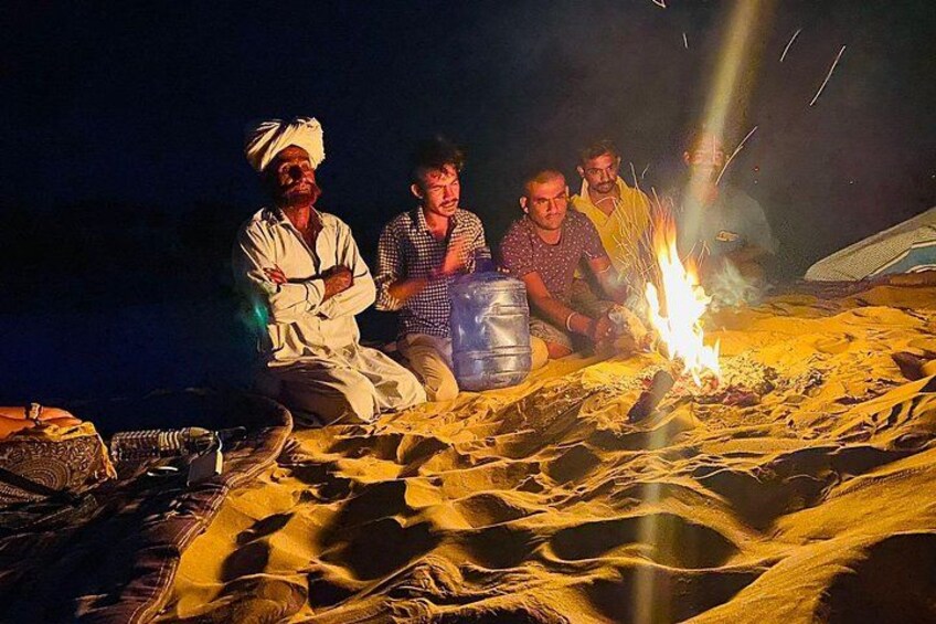 Un grupo de personas sentadas alrededor de una fogata en una playa arenosa de noche. 4