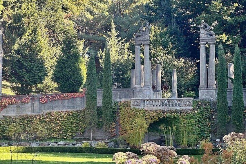 A stone bridge with columns, surrounded by greenery and trees. 1