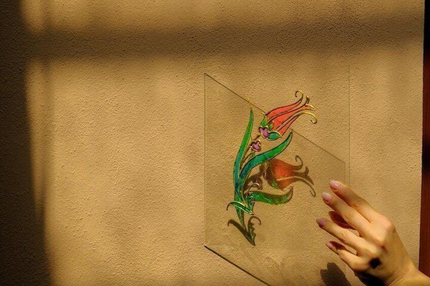 A hand holding a transparent glass with a colorful floral design. 5