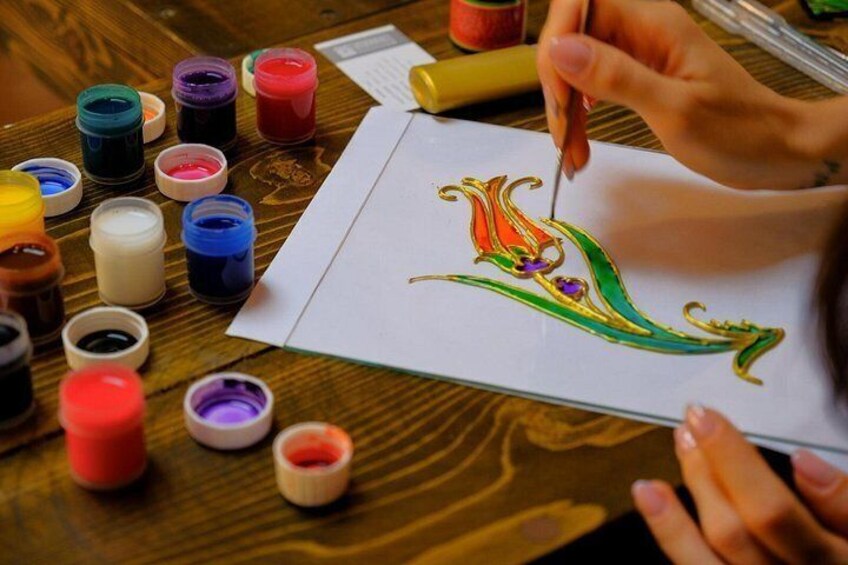 A person painting a colorful design on paper with various paint containers around. 2