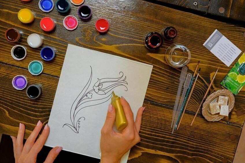 A person drawing on paper with various colored paints and brushes on a wooden table. 3