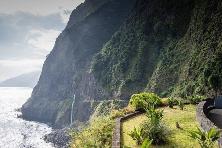 Una scogliera costiera con una cascata, vegetazione rigogliosa e un sentiero in pietra. 3