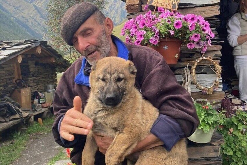 A person holding a dog in a rustic outdoor setting with wooden structures and potted plants. 4