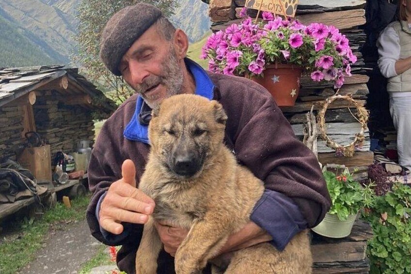 Een persoon met een hond in een landelijke omgeving, met een houten constructie en bloempotten op de achtergrond. 4
