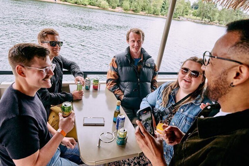 A group of people sitting at a table by a lake, holding drinks and a camera. 1