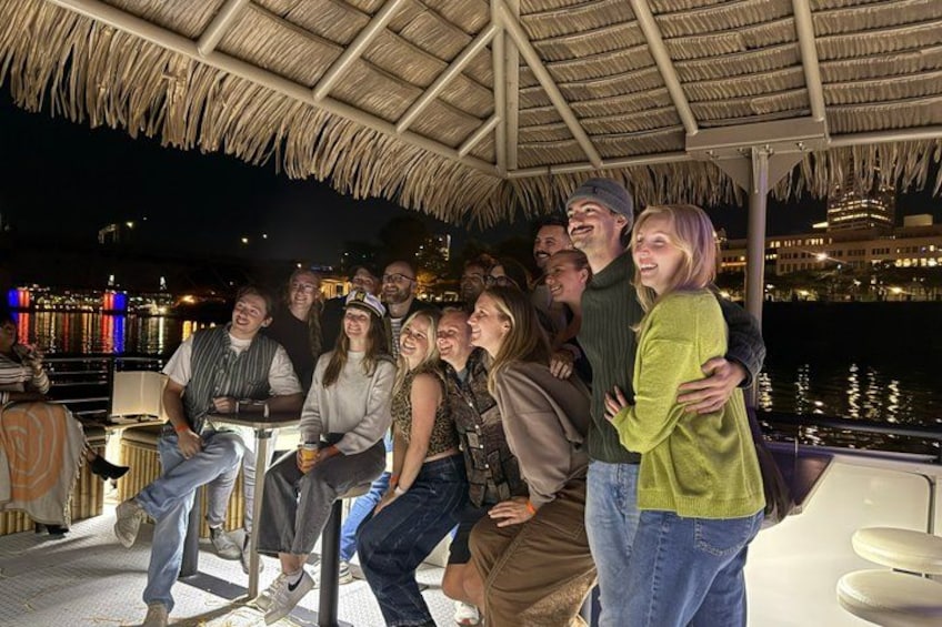A group of people gathered under a thatched roof structure by a waterfront. 5