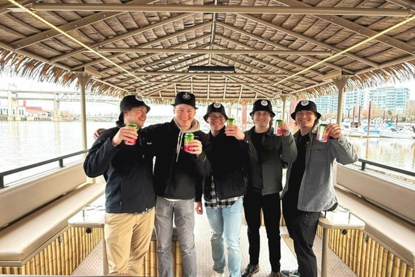 A group of people on a boat with a thatched roof, holding drinks. 4