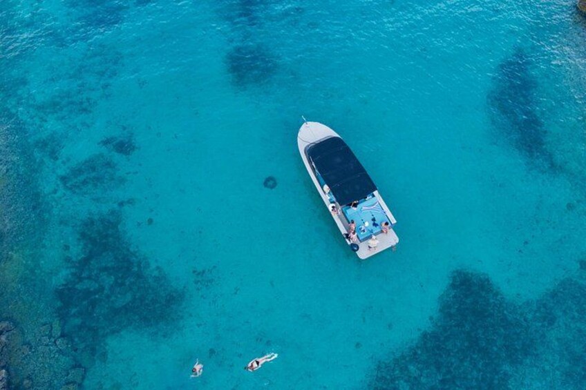 A boat anchored in clear turquoise water with two people swimming nearby. 2