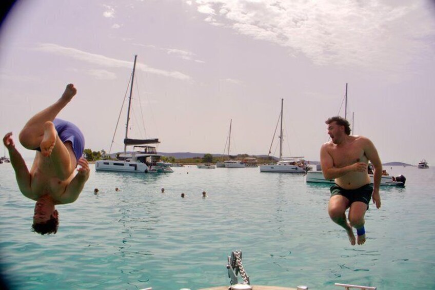 Two people diving into the water with sailboats in the background. 3