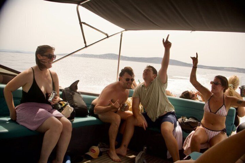 People on a boat, some sitting and some standing, with a body of water and distant land in the background. 5
