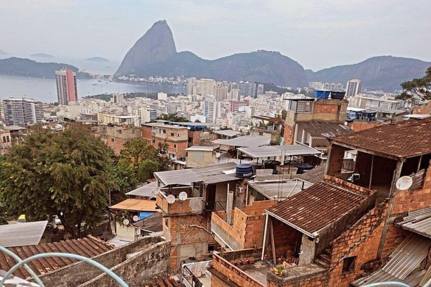 Paesaggio urbano con una montagna imponente sullo sfondo, un mix di edifici residenziali e commerciali, e un corpo d'acqua. 1