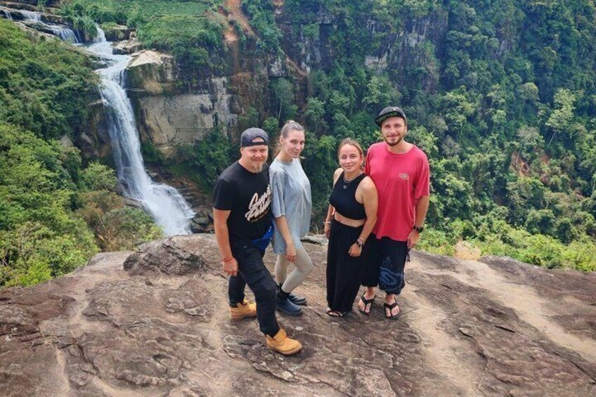 Eine Gruppe von Menschen steht auf einer Felsformation, im Hintergrund ein Wasserfall. 4