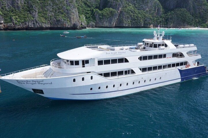 A large white boat named 'Sea Angel Seyong' on clear turquoise waters with a rocky coastline in the background. 1