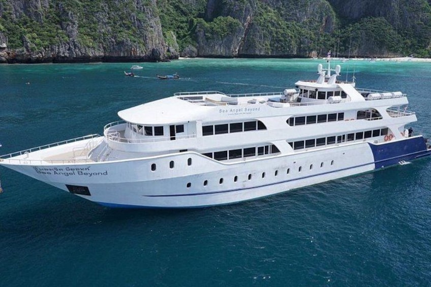 Un barco blanco grande llamado 'Sea Angel Beyond' en aguas turquesa cristalinas con acantilados rocosos al fondo. 1