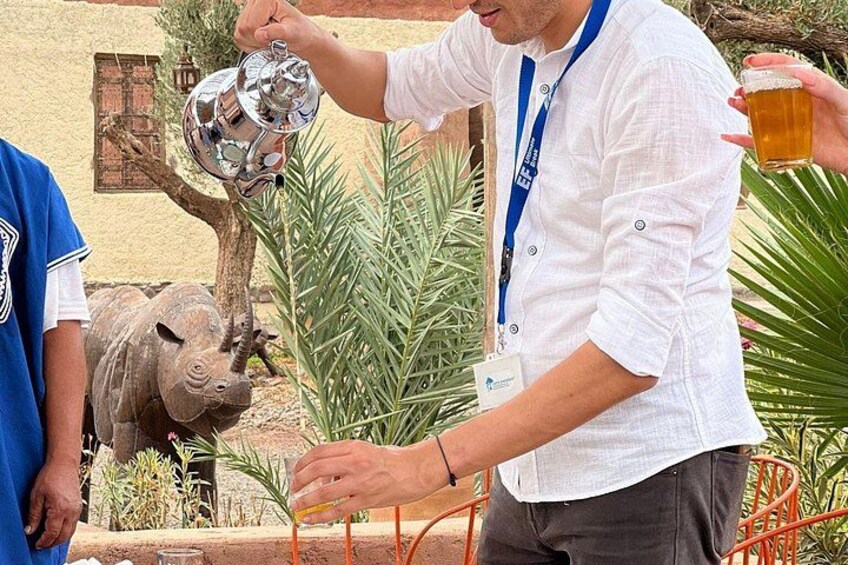 A person pouring beer from a metal pitcher into a glass, with a decorative bull sculpture and plants in the background. 2
