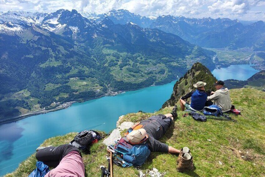 People resting on a mountain ledge overlooking a lake and mountains. 2