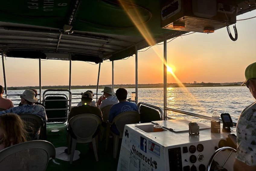 A boat with people seated at tables, a sunset in the background, and a calm sea. 1