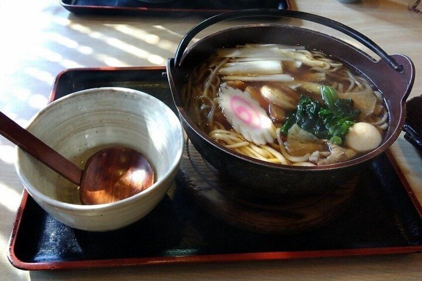 A bowl of soup with noodles, vegetables, and a dumpling on a tray. 2